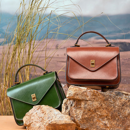 Brown and green leather messenger bags displayed on rocks with desert backdrop