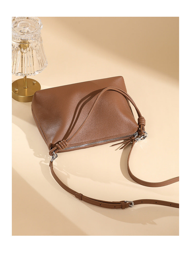 Caramel pebbled leather tote with adjustable strap laid flat near a table lamp