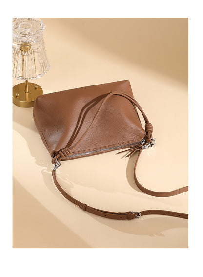 Caramel pebbled leather tote with adjustable strap laid flat near a table lamp