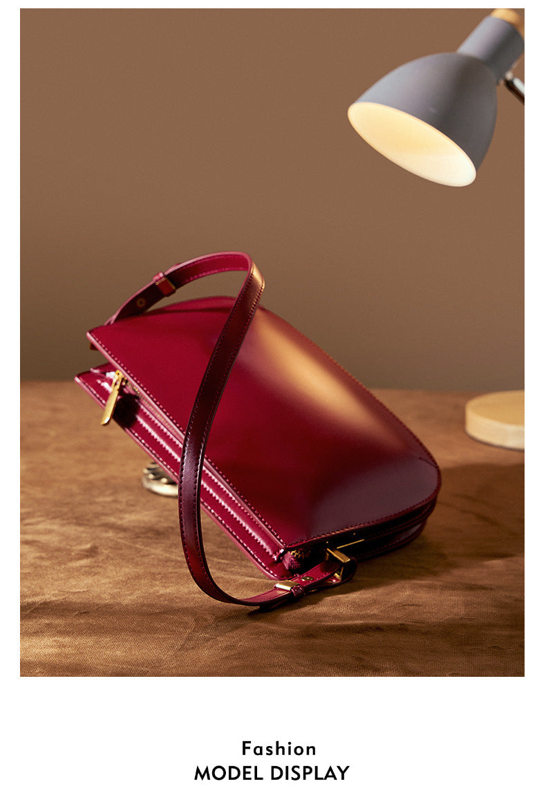 Burgundy leather underarm bag angled on a brown surface under a desk lamp, Fashion Model Display