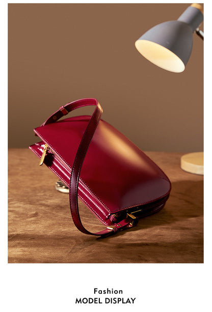 Burgundy leather underarm bag angled on a brown surface under a desk lamp, Fashion Model Display