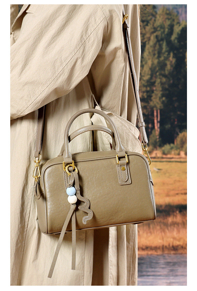 Close-up of a taupe leather pillow bag worn crossbody against a beige trench coat