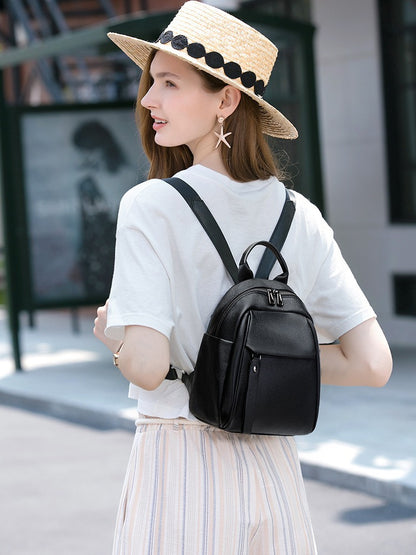 Woman wearing a black top-grain cowhide backpack with front zip pocket and adjustable shoulder straps