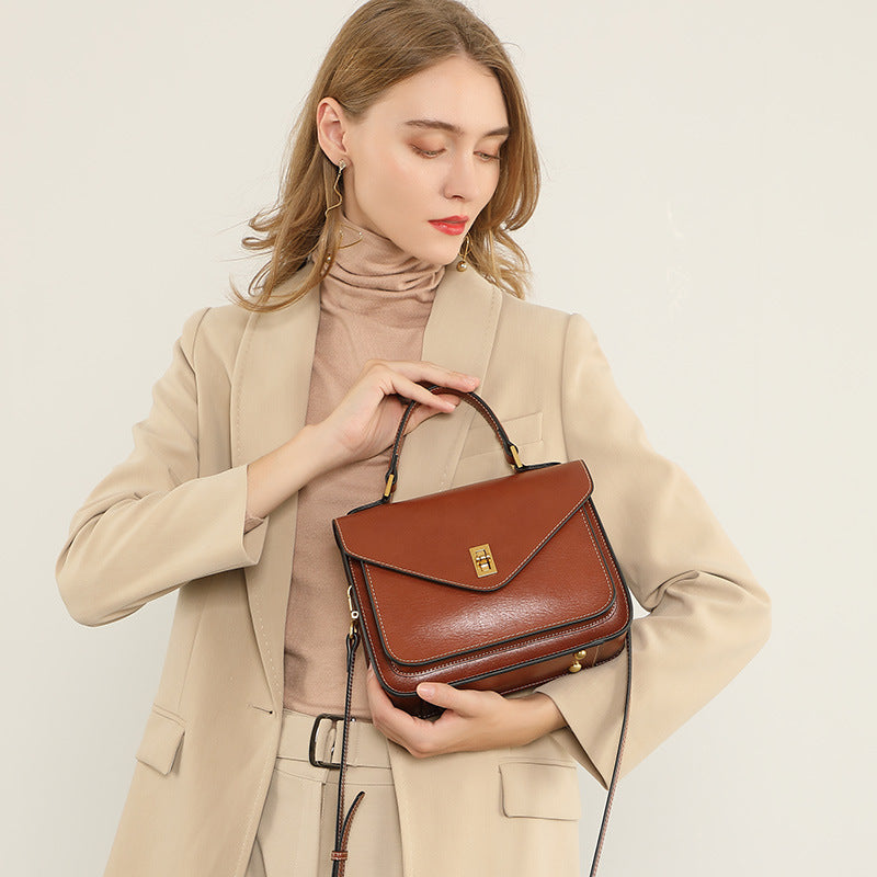 Woman in beige blazer holding brown leather messenger bag by the top handle