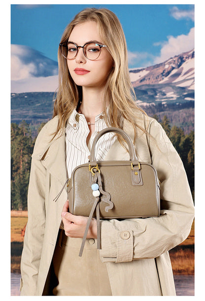 Model in a beige trench coat holding a taupe leather pillow bag at her side