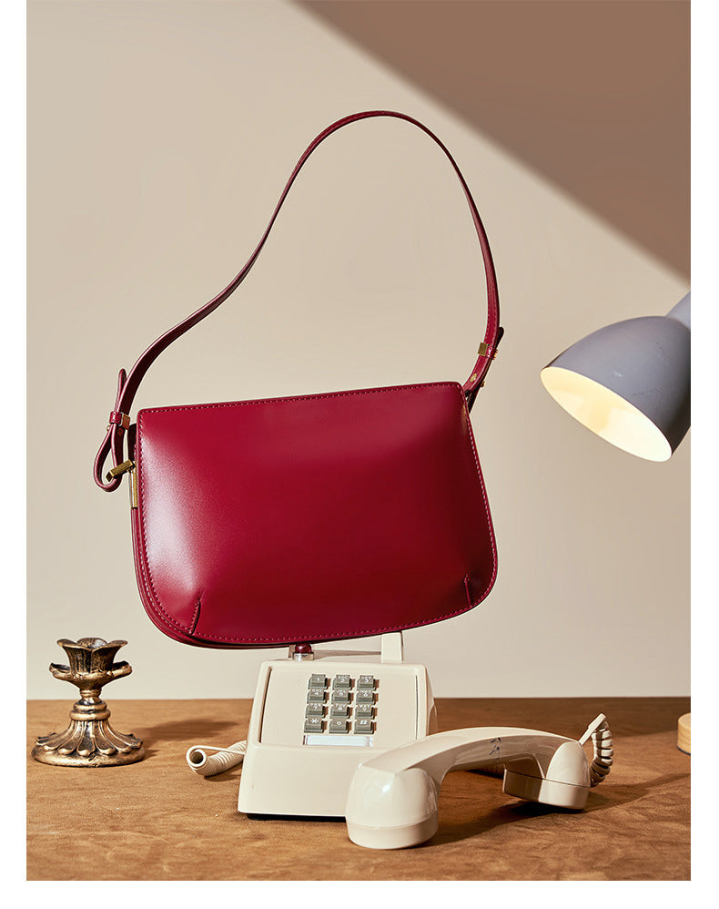 Styled scene of the burgundy leather underarm bag on a desk with a vintage push-button telephone
