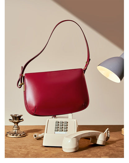 Styled scene of the burgundy leather underarm bag on a desk with a vintage push-button telephone