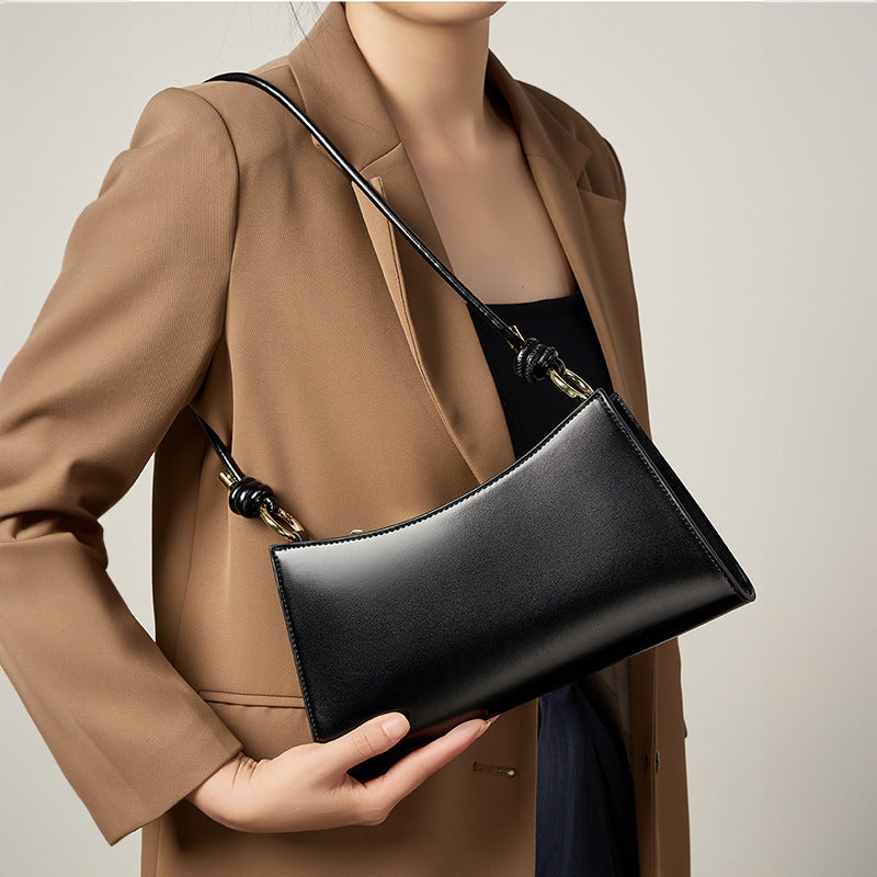 Black leather shoulder bag tucked under the arm with a camel coat