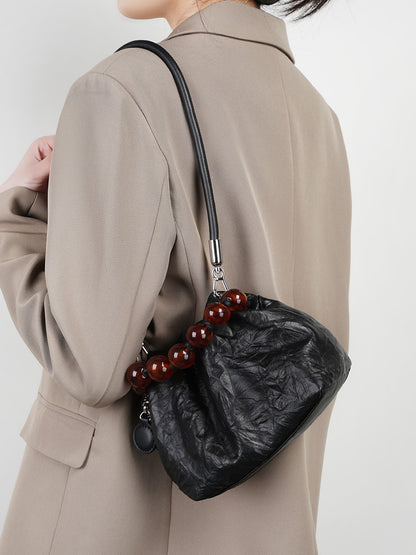 Black crinkle bag worn under the arm with chain strap against a beige coat