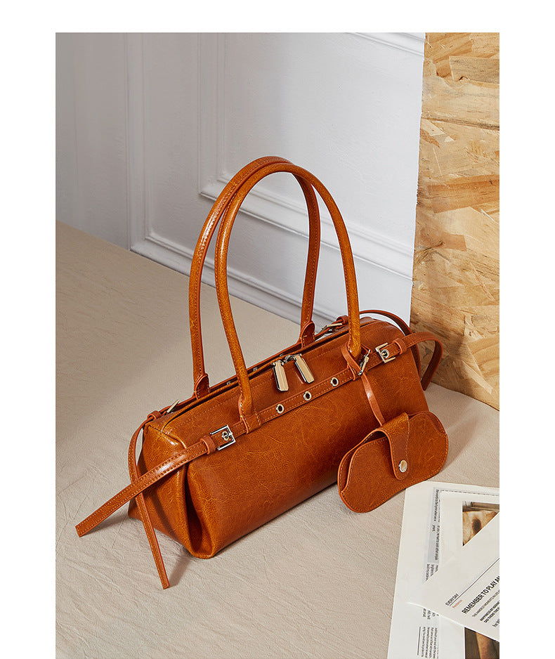 Tan leather barrel bag styled on beige surface with paper and wood accents