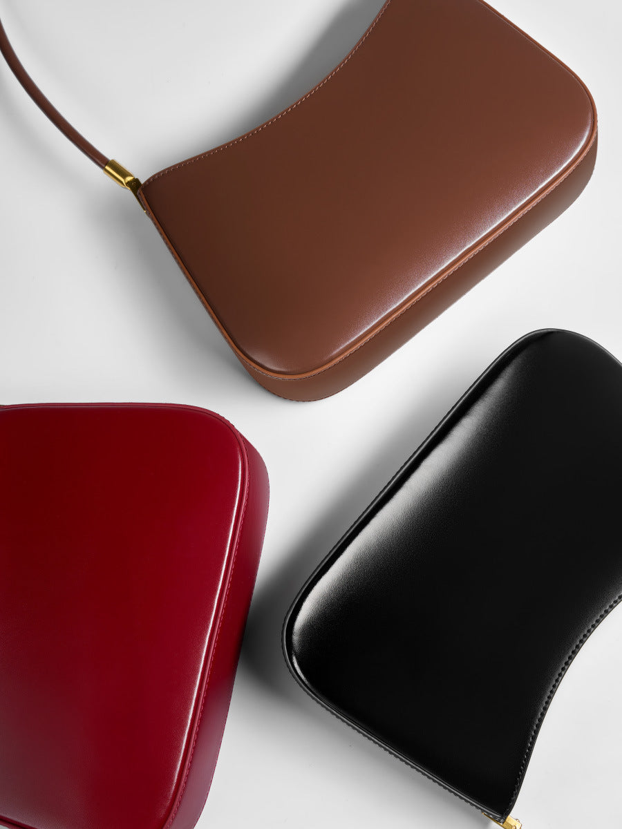 Flat lay of three cowhide shoulder bags in coffee, wine red, and black