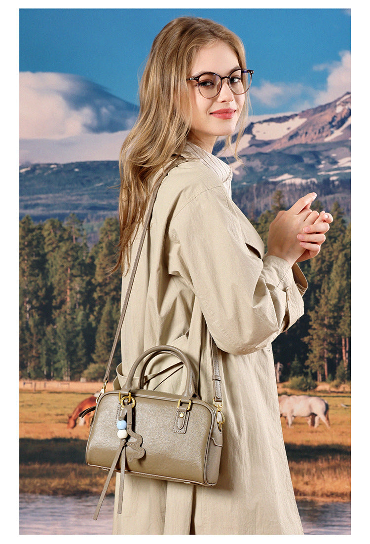 Model in a beige trench coat carrying a taupe leather pillow crossbody bag outdoors