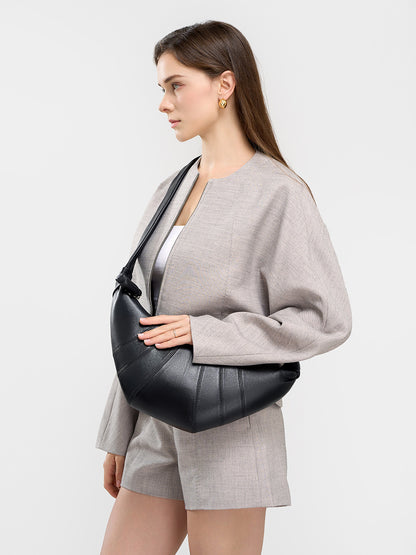Model carrying black crescent bag under the arm in casual gray outfit
