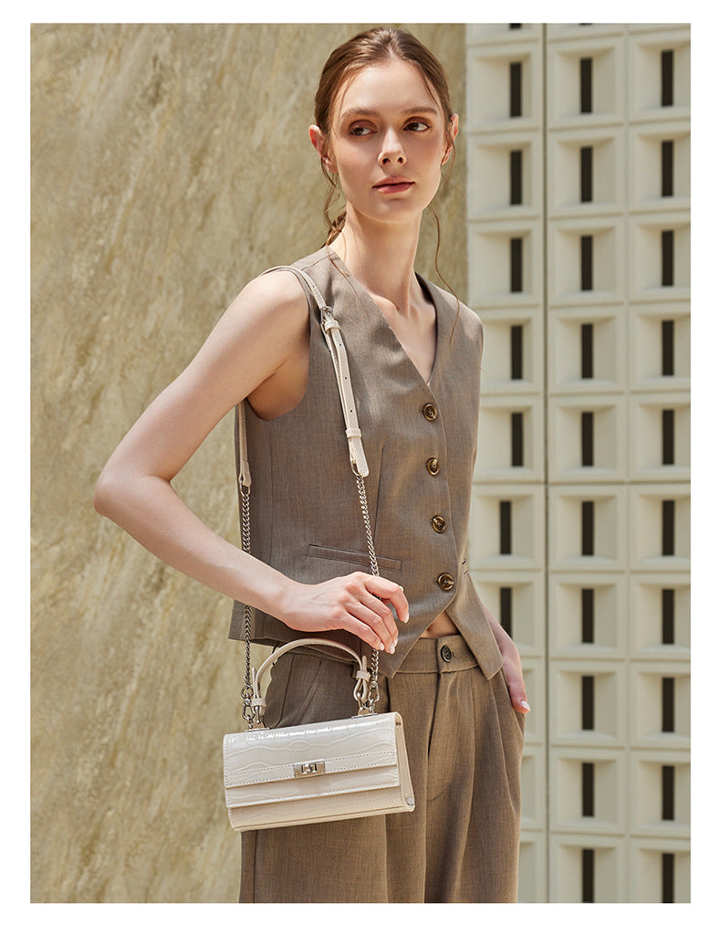 Model carrying the cream white croco-embossed bag crossbody with chain strap outdoors