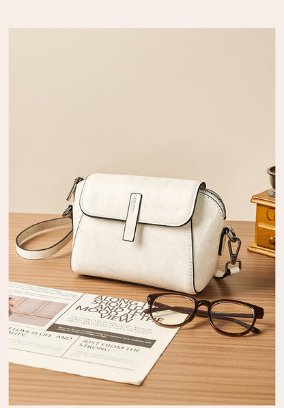 Milk white crossbody bag styled with sunglasses and newspaper on wood
