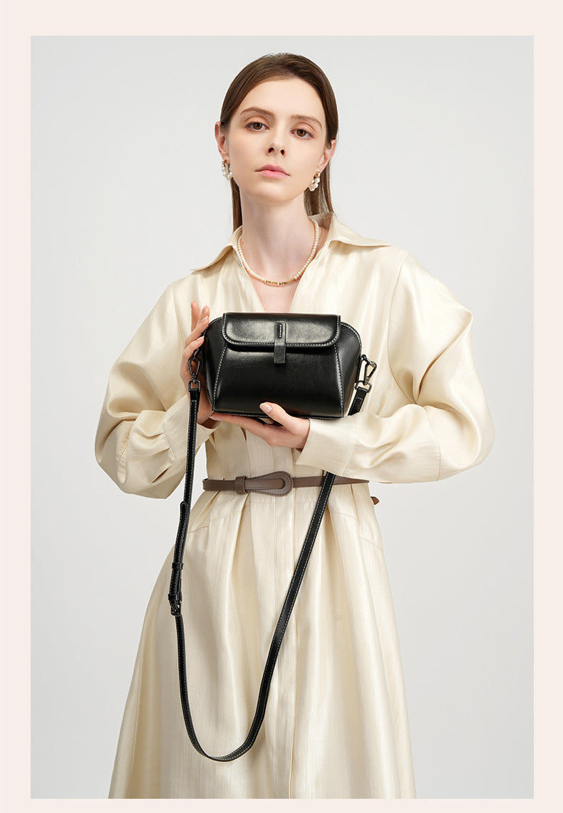 Model presenting a black leather crossbody bag in both hands