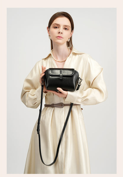 Model presenting a black leather crossbody bag in both hands