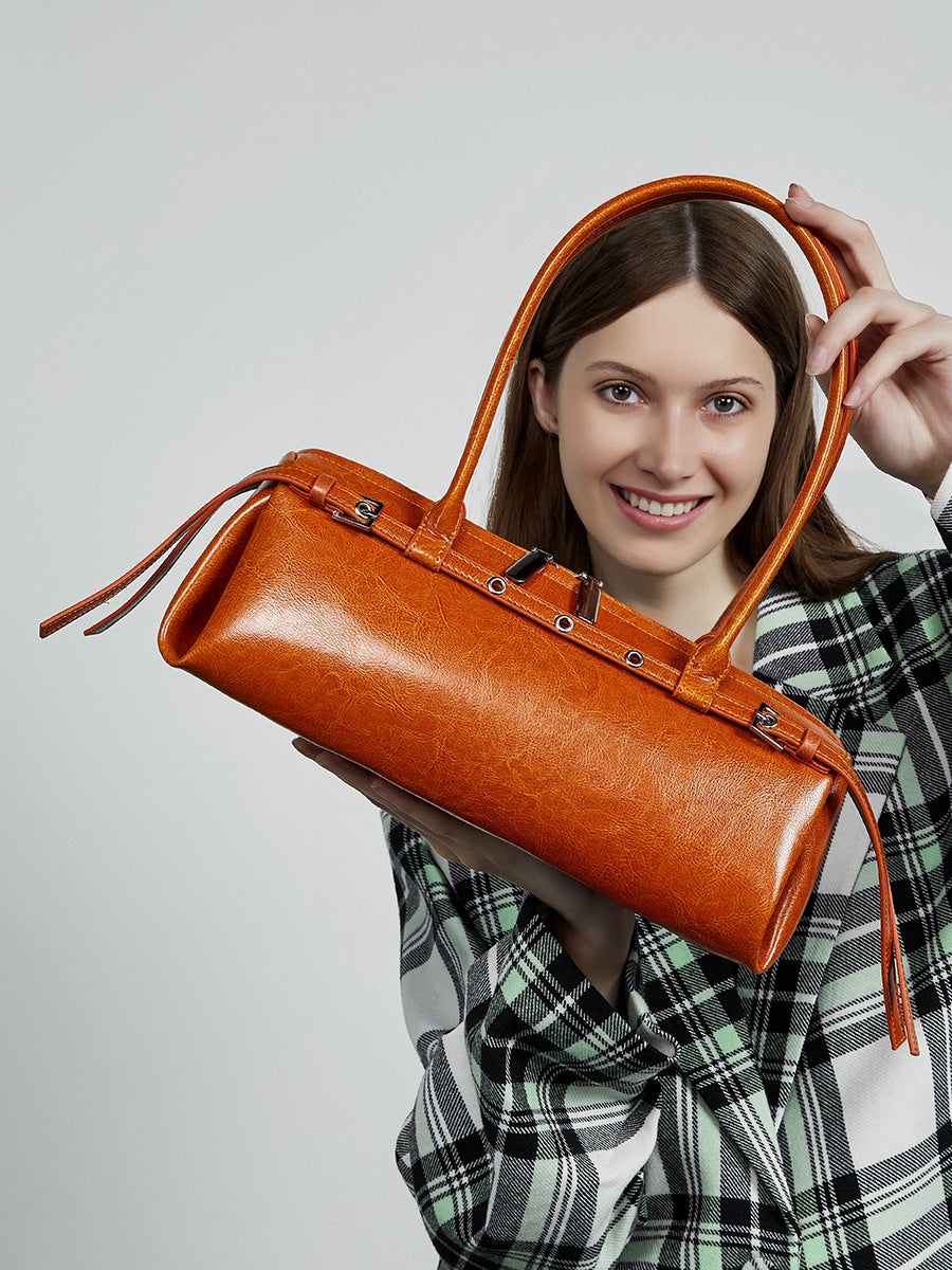 Model in green plaid shirt carrying tan leather barrel tote in hand