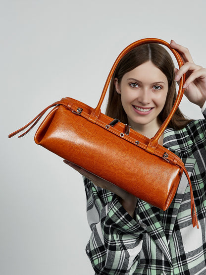 Model in green plaid shirt carrying tan leather barrel tote in hand