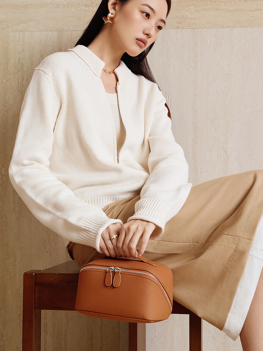 Brown leather cosmetic pouch held by a model in a cream knit cardigan, styled for daily wear