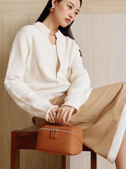 Brown leather cosmetic pouch held by a model in a cream knit cardigan, styled for daily wear