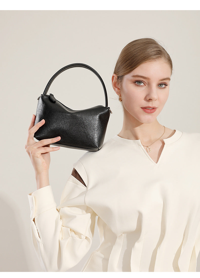 Black leather pillow bag held up close by a model