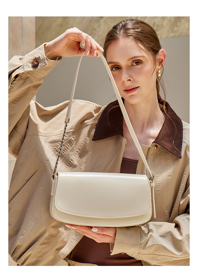 Model holding an off-white baguette bag by the strap in a soft portrait