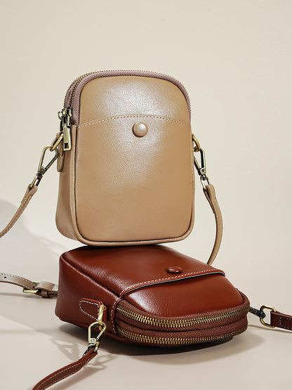 Apricot and caramel cowhide leather crossbody bags stacked, showing strap and hardware