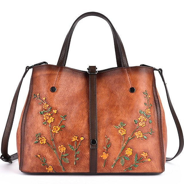 Front view of a vintage brown leather tote with floral detailing and shoulder strap