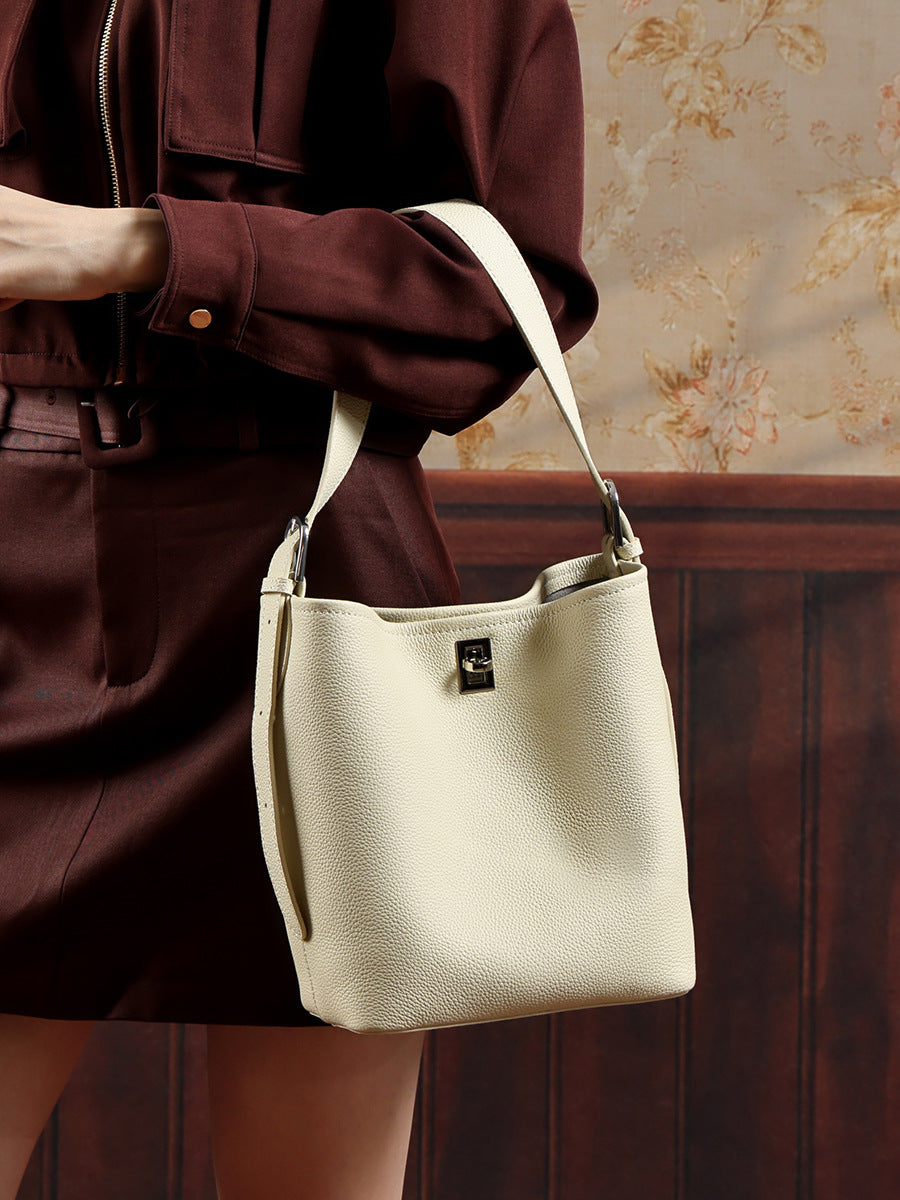 Close-up of off-white leather bucket bag held as a shoulder bag against a dark brown outfit