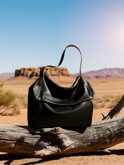 Black leather tote bag resting on a fallen log with mesas in the background
