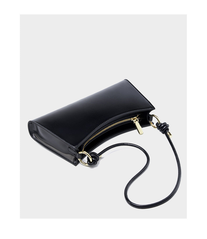 Black leather underarm bag with strap extended showing gold-tone rings and knots