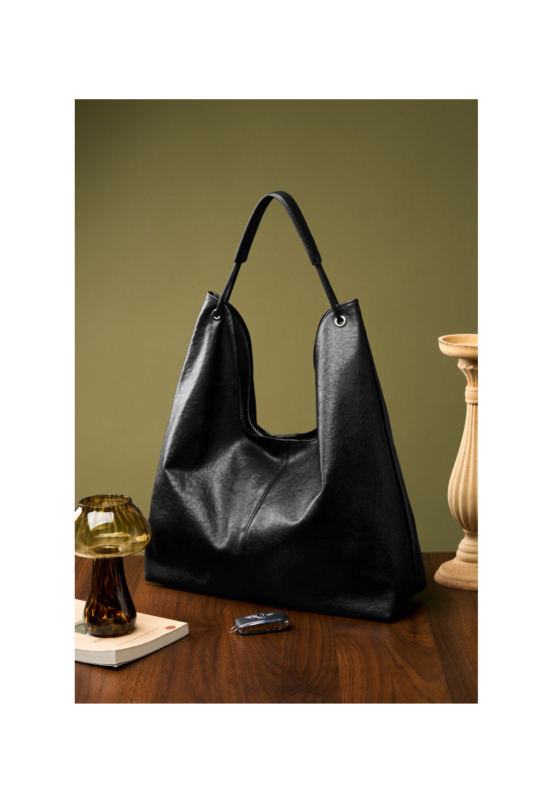 Black hobo tote bag styled on a wooden surface with amber glass vase