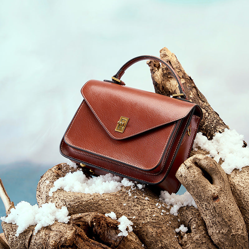 Brown leather messenger bag styled outdoors on driftwood with snow detail