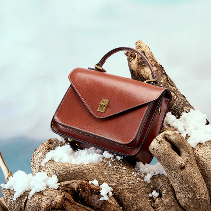Brown leather messenger bag styled outdoors on driftwood with snow detail