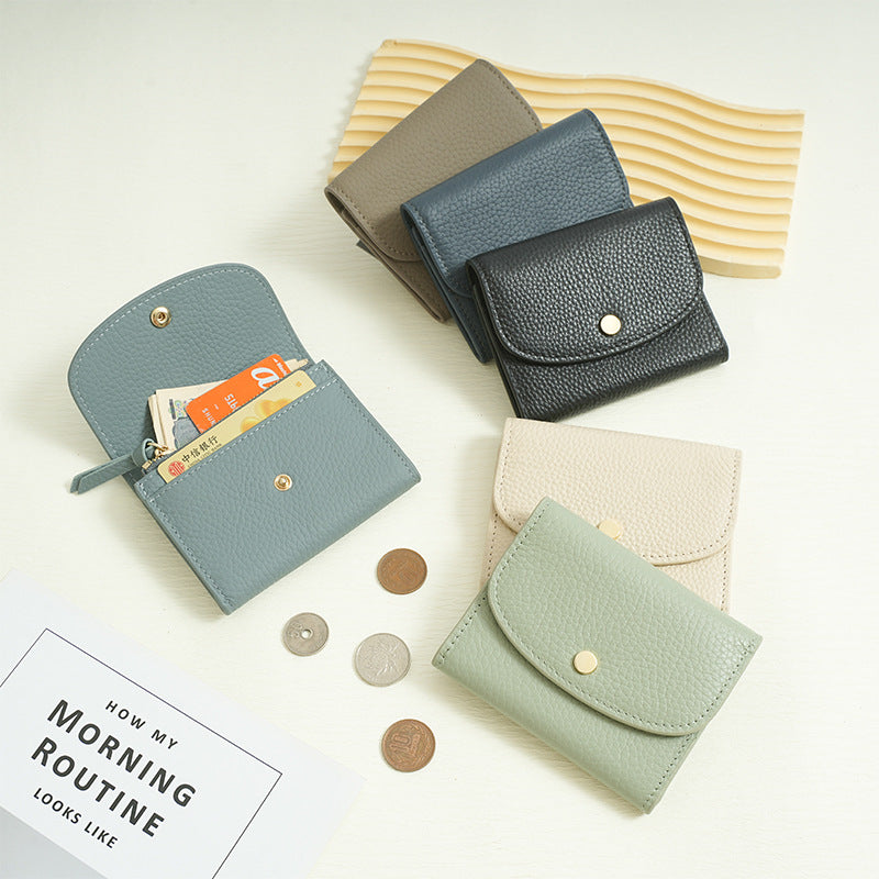 Five color variants of the cowhide mini coin purse wallet displayed on a tabletop with coins and currency