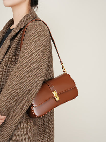 Side angle of coffee brown cowhide leather baguette bag worn over the shoulder with gold hardware