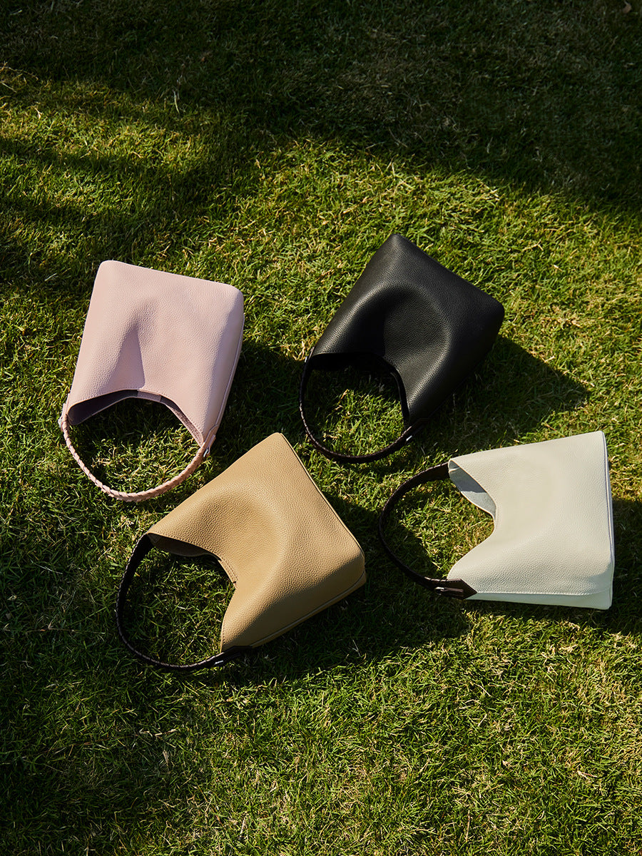 Four leather bucket bags in pink, black, grey and white arranged on grass