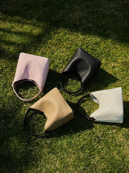 Four leather bucket bags in pink, black, grey and white arranged on grass