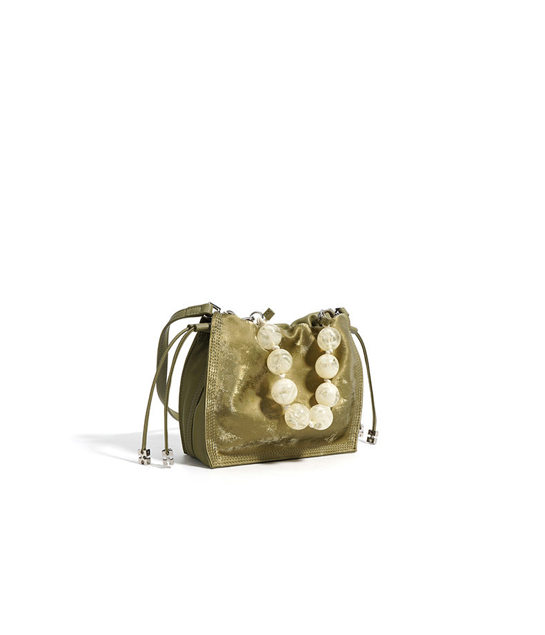 Detail view of champagne mini bucket bag beaded handle and metallic surface