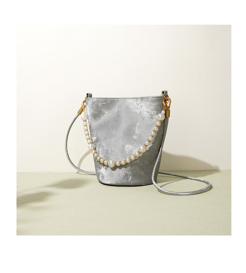 Silver gray mini bucket bag with pearl chain on a green surface