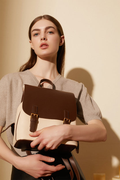 Model holding the two-tone backpack against her chest, showing the front flap and buckle detail