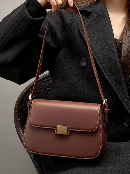 Caramel leather shoulder bag held by strap, showing side profile and hardware