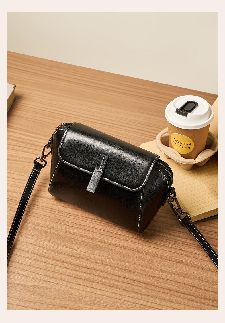 Black leather crossbody bag on wooden desk next to takeaway coffee