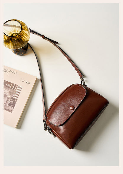 Flat lay of brown leather crossbody bag with book and amber glass