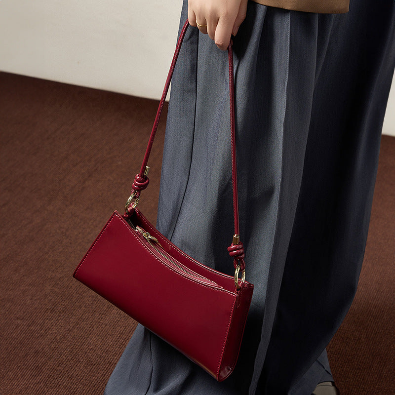 Wine red leather shoulder bag carried by hand against wide-leg trousers