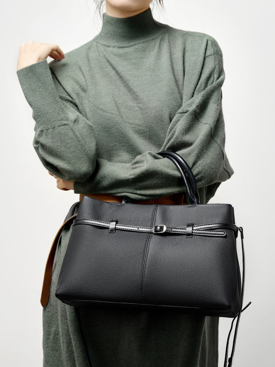 Model in green sweater holding black pebbled leather tote