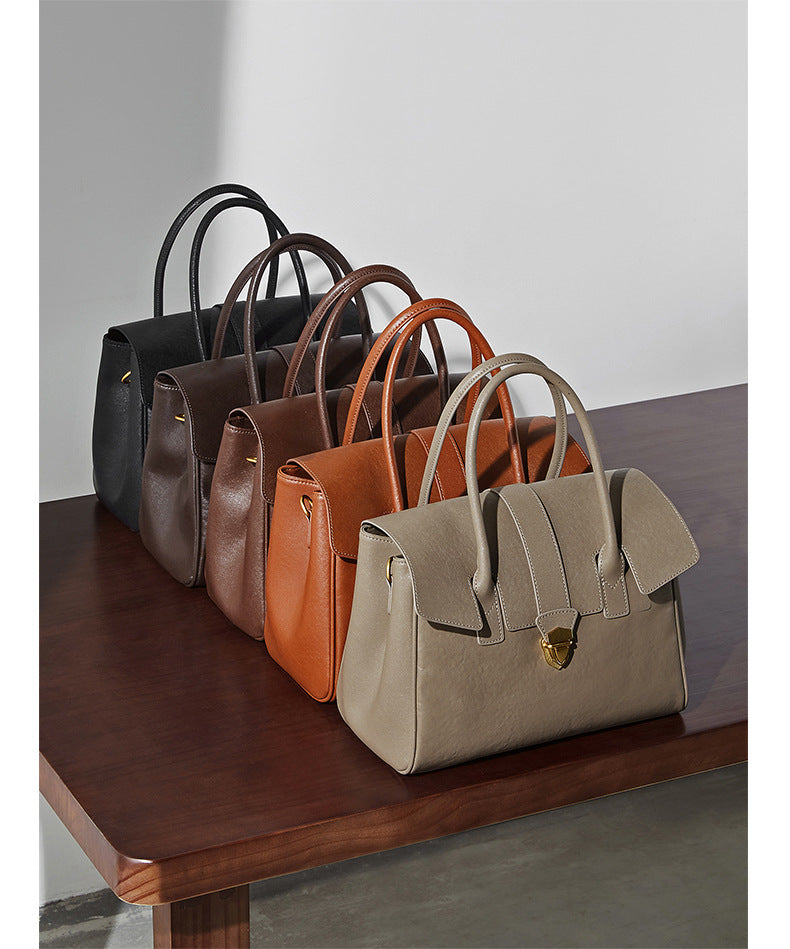 Five leather satchel bags in different colors arranged on a table