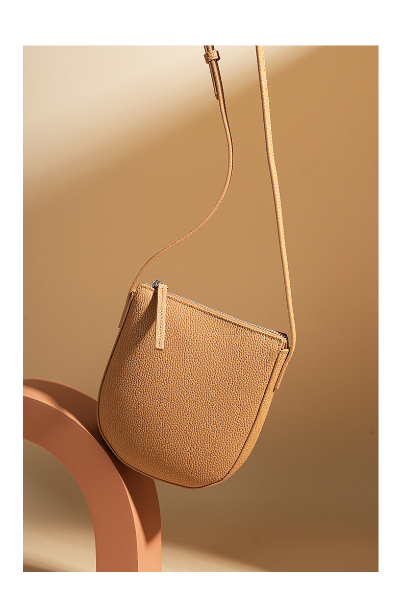 Biscuit cowhide leather crossbody bag styled on beige pedestal with strap extended