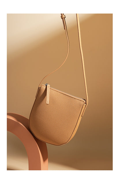 Biscuit cowhide leather crossbody bag styled on beige pedestal with strap extended